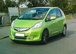 Grüner Honda Jazz Hybrid im Straßenverkehr. 