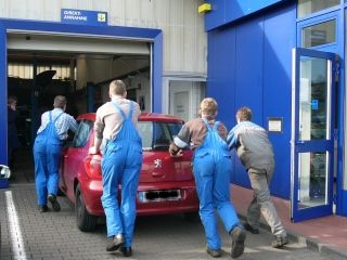 Vier Mitarbeiter schieben den Peugeot 307 in die Werkstatt. 