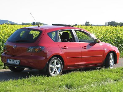 Roter Mazda3 vor einem Rapsfeld. 