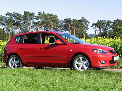 Roter Mazda3 vor einem Rapsfeld. 