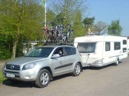 RAV4 mit angehängtem Wohnwagen und vier Fahrrädern auf dem Dachträger. 