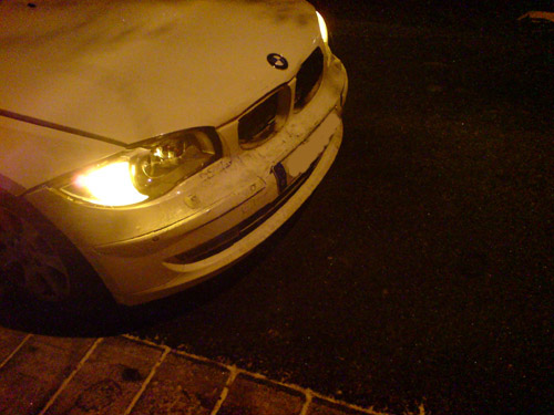 Motorhaube, Kotflügel rechts, Scheinwerfer, Stoßstange und Kleinteile sind verbeult oder verteilen sich über die Straße. Verbeulte Front des 1er BMWs.