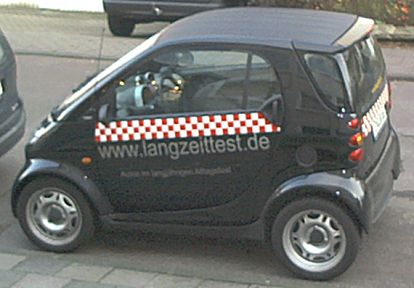 Der schwarze smart fortwo von Oliver Riesen mit seiner rot-weißen Bauchbinde und den Werbeaufklebern. 