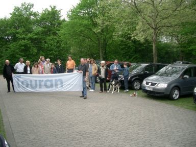 Die Teilnehmer des Touran-Treffens vor ihren Fahrzeugen mit einer großen Touranflagge. 
